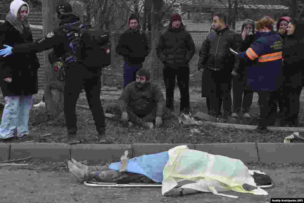 A man sits dejectedly as bystanders react to the death of a woman killed in the air attack in Zaporizhzhya. 