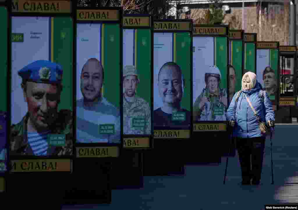 A woman walks by billboards in Bucha of Ukrainian soldiers who died defending their country.
