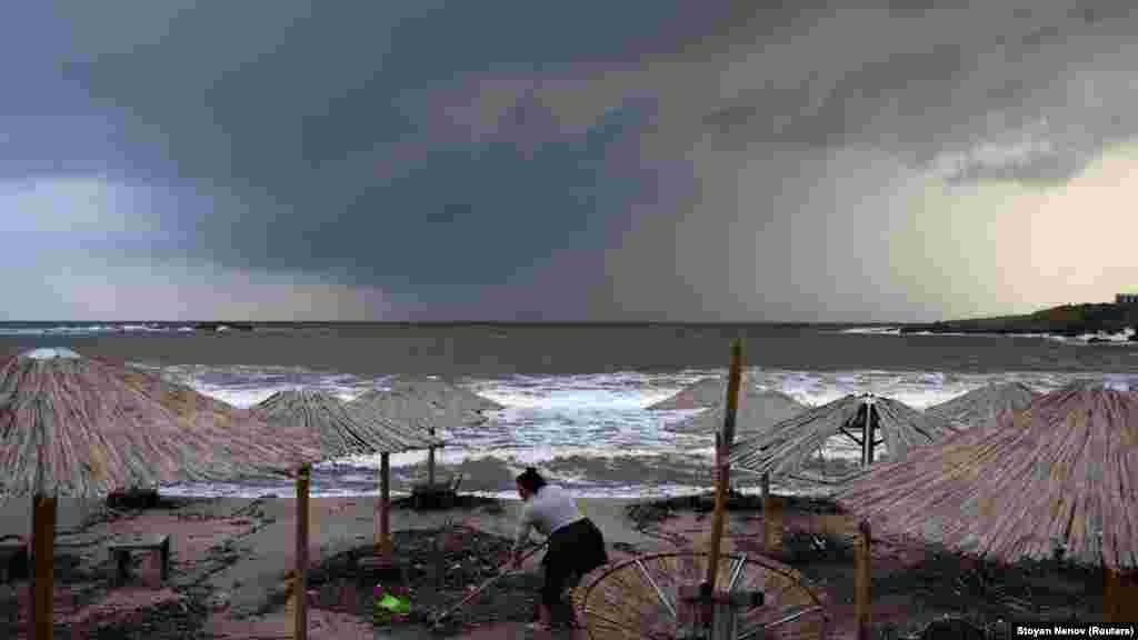 A woman cleans debris on the beach. 
