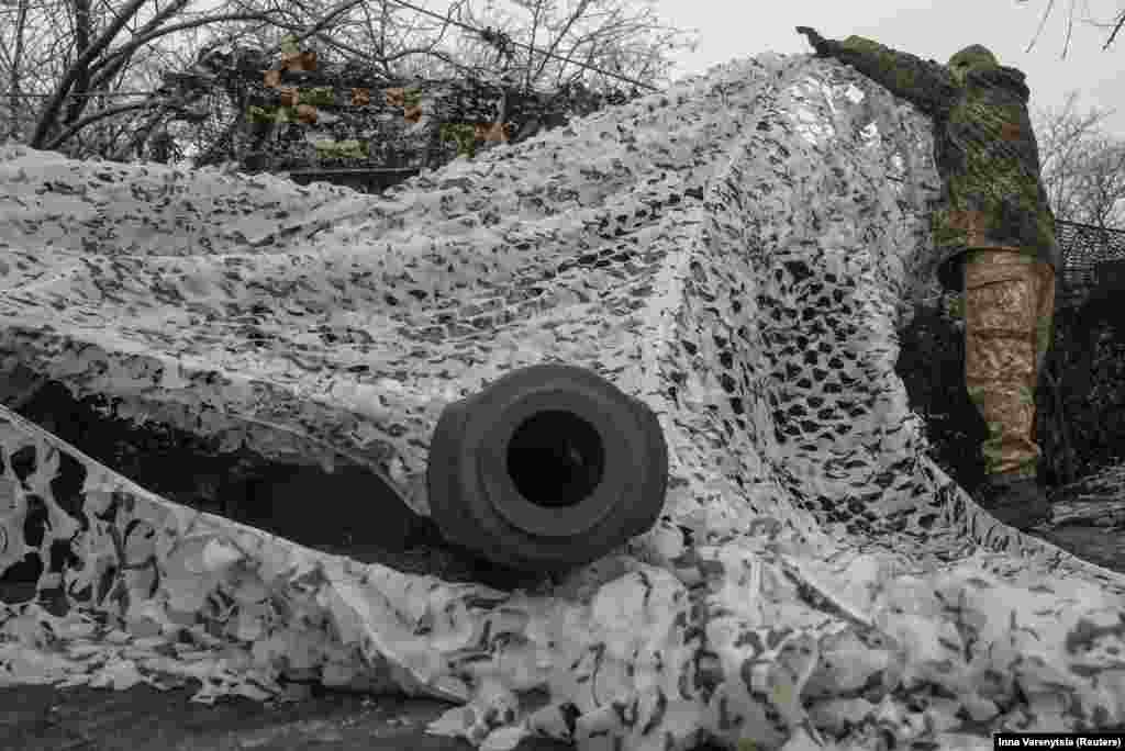 A soldier adjusts the camouflage above a 2S1 Gvozdika self-propelled howitzer. 