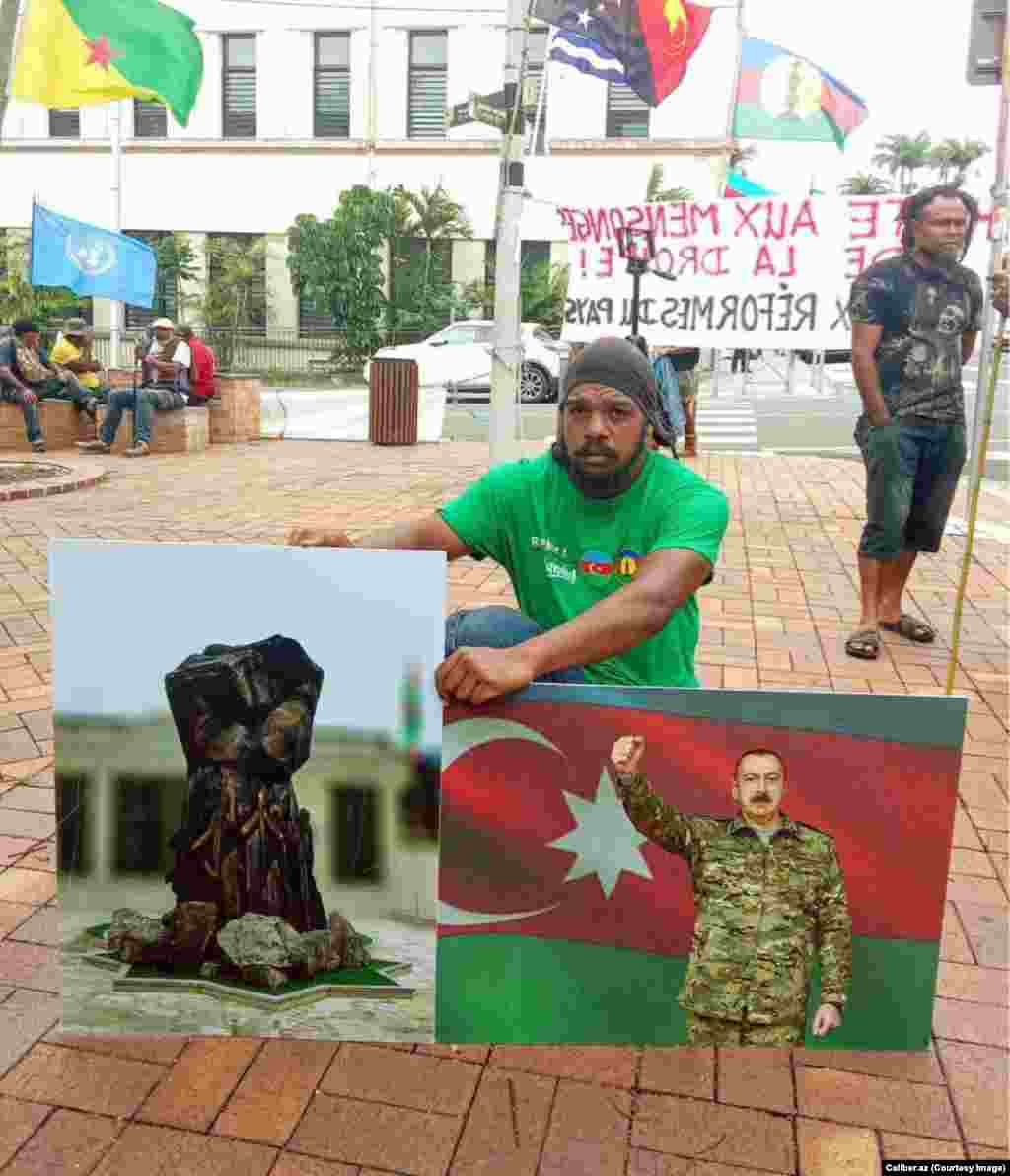A protester in Noumea is photographed in March holding pictures of Azerbaijani President Ilham Aliyev and of an Azerbaijani war memorial. The pictured memorial was recently unveiled in Azerbaijan's retaken Kalbacar district. 