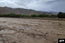 Residents stand next to a river covered with mud after flash floods in the village of Logariha in the Nahrin district of Baghlan Province on May 10.