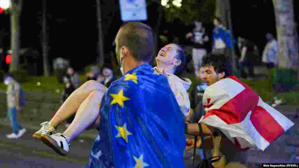A man draped in an EU flag carries an injured protester. Supporters of the bill say it mirrors similar U.S. legislation and promotes transparency. Opponents say the proposed legislation would stifle dissent and silence independent media. They have compared it to similar legislation in Russia, which is why many call it the "Russian law." 