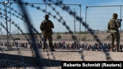 U.S. soldiers watch migrants waiting on the U.S. side of the border to be allowed to go to a CBP processing center in El Paso, Texas.