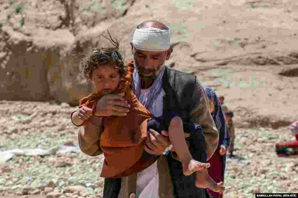 Carrying a child, Salim, a 45-year-old man from Baghlan who lost four of his family members in the flash flooding, visits the graves of his relatives in the village of Sherjalal.