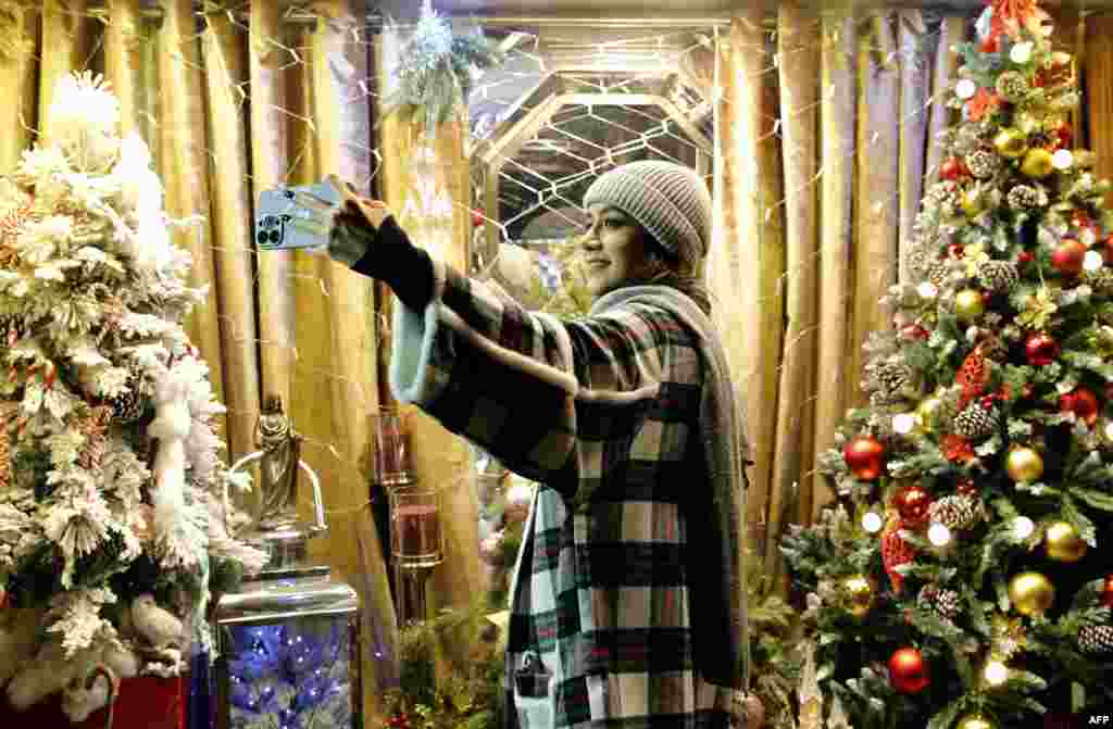A young Iranian woman takes a selfie in front of Christmas trees in Tehran on December 25. In recent years, women deemed by the country's morality police to be flouting head-covering laws were made to attend a lecture on "Islamic values." A family member was then permitted to collect them for release.