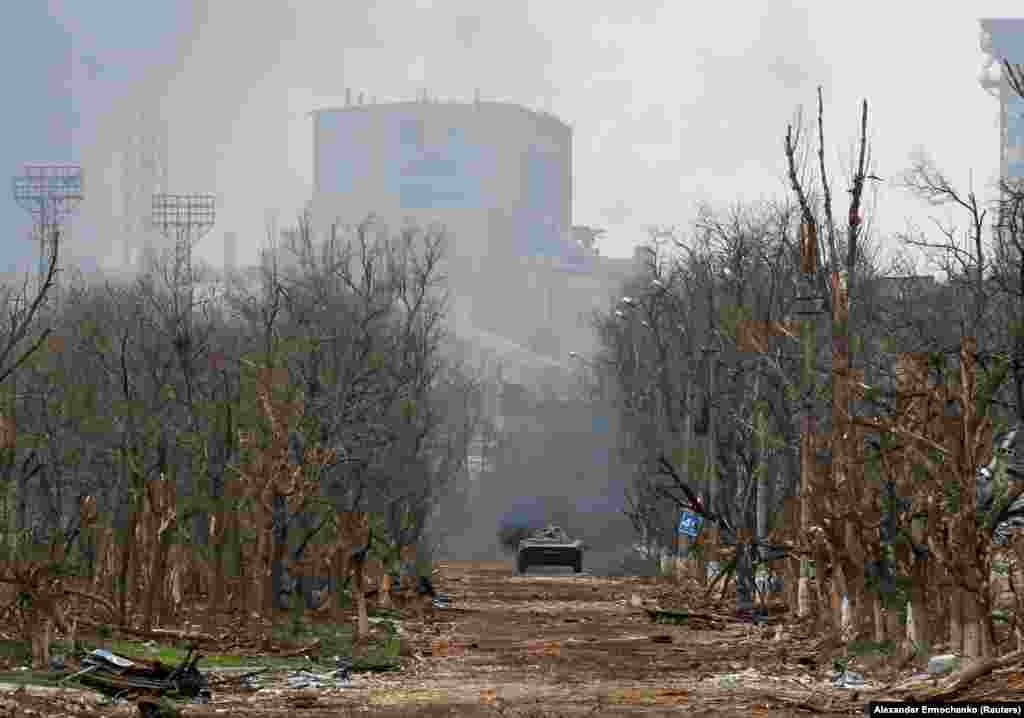 An armored vehicle of Russia's forces moves down a war-ravaged street in Mariupol on April 12. The massive Soviet-era Azovstal iron and steel works rises in the background. 