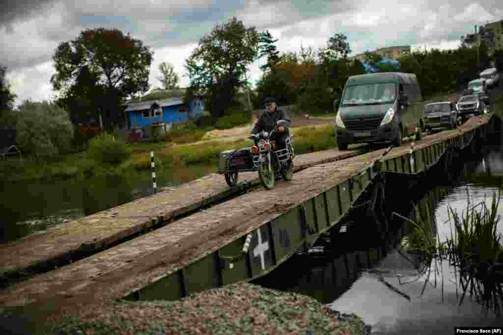 Locals and army vehicles cross a temporary bridge in Izyum that replaced one nearby which had been destroyed. 