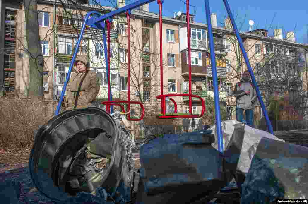 A man and a woman stand next to fragments of military equipment on the street in the aftermath of an apparent Russian air strike in Kharkiv.