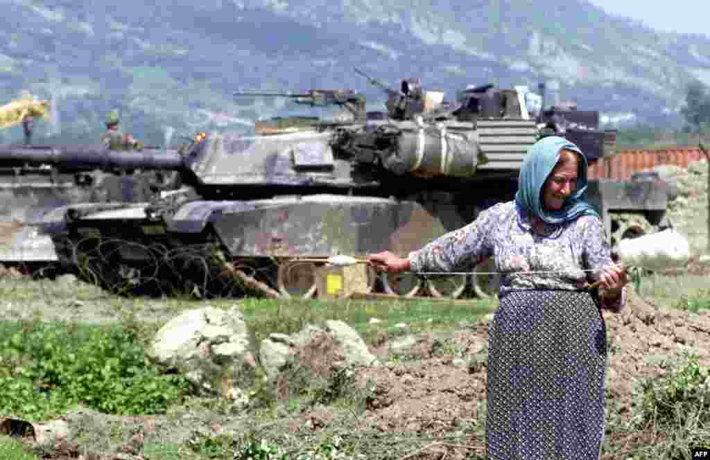 An Albanian woman spins wool in front of a U.S. M1 Abrams tank that was part of NATO's operation during the Kosovo conflict, outside the Rinas airbase on May 12, 1999. With a crew of four (commander, gunner, loader, and driver), the Abrams is one of the heaviest tanks in service at nearly 62 metric tons. 