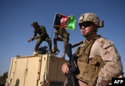 A U.S. Marine looks on as Afghan National Army soldiers raise the Afghan national flag on an armed vehicle during a training exercise to deal with improvised explosive devices in 2017.