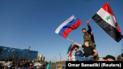 Сирийцы размахивают сирийскими и российскими флагами, протестуя против ракетных ударов США и их союзников, 14 апреля 2018