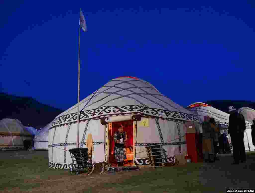A woman leaves her yurt with a pile of dishes as the games' attendees settle in for the night in the chilly mountain venue.