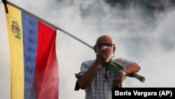 An opponent of President Nicolas Maduro carrying a Venezuelan flag covers his face amid tear gas fired by soldiers loyal to Maduro during an attempted military uprising to oust Maduro in Caracas on April 30.