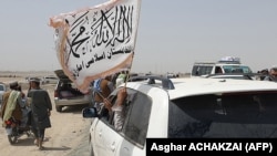 People wave a Taliban flag as they drive through the Pakistani border town of Chaman on July 14, after the Taliban claimed it had captured the Afghan side of the border crossing at Spin Boldak.