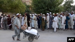 د شمالي وزیرستان یو وګړی په بنو کې د ملګرو ملتونو د خوړو ادارې ورکړې مرستې کور ته لېږدوي. ورسره، ګڼ کسان د مرستو ترلاسه کولو لپاره په قطار کې ولاړ دي - پخوانی انځور.