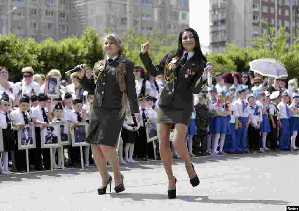 Women in military uniforms sing and dance at the parade.