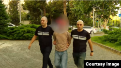 მკვლელობის მცდელობისთვის დაკავებული კაცი პოლიციის შენობაში მიჰყავთ.