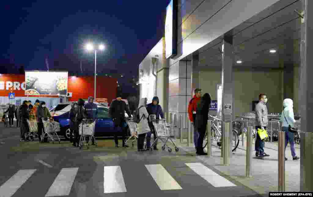 People queue at the entrance of a supermarket while keeping a safe distance from one another in Bucharest, Romania. Romanian President Klaus Iohannis announced a lockdown across the country on March 25 and asked the army to help enforce the new measures. 