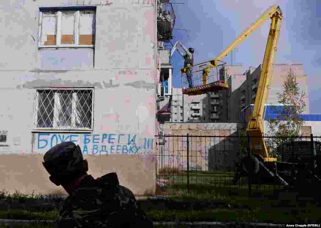 A Ukrainian soldier walks past as van Helten is lifted into position. The graffiti, in Russian, reads "God Save Avdiyivka." 