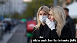 Two women wearing face masks wait to cross the road in the center of in Moscow.