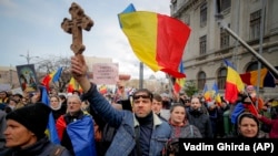 An anti-vaccination protester holds a wooden cross as others wave national flags during a rally in Bucharest in March 2021.