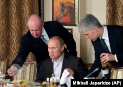 Prigozhin (left) and then-Russian Prime Minister Vladimir Putin (center) during a dinner with foreign scholars and journalists outside Moscow in November 2011.