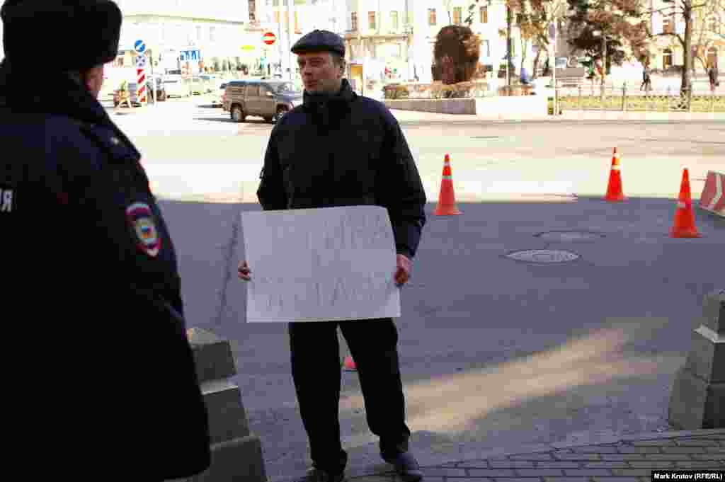 Мужчина с плакатом "Путина в отставку" внезапно появился в нескольких метрах от пикетчиков и тут же был задержан полицией. Был ли он провокатором, чья роль - нарушить правила проведения одиночных пикетов, осталось неясным