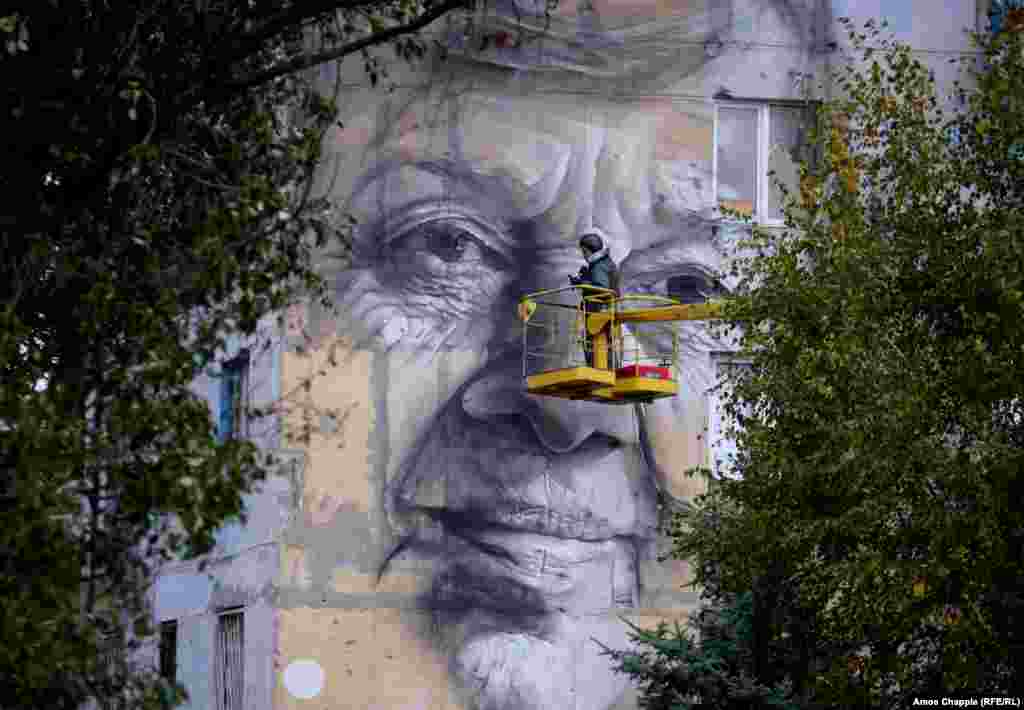 Wearing a flak jacket and ballistic helmet, Guido van Helten nears completion of his portrait of a local woman. 