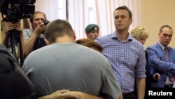 Pyotr Ofitserov (with back to camera) gives his wife a farewell embrace as Aleksei Navalny (facing camera) awaits custody after the verdict in the courtroom in Kirov on July 18.