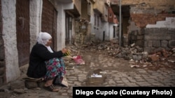 A woman knits in front of a home that was destroyed by a bomb during fighting in Sur.