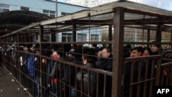 Migrant workers line up in a fenced holding area outside the Federal Migration Service office as they wait for their turn to get a work permit.