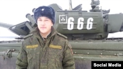 A Russian soldier stands next to a T-72B3 tank with the tactical sign of the 6th Tank Division.