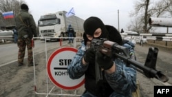 Armed masked men who describe themselves as members of Ukraine's disbanded elite "Berkut" police force at a checkpoint under Russian national and Russian naval flags on a Crimean highway.