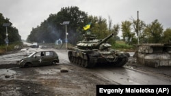 Украинский танк проезжает мимо бывшего российского контрольно-пропускного пункта в городе Изюм Харьковской области, ранее освобожденного Вооруженными силами Украины от российской армии, 16 сентября 2022 года