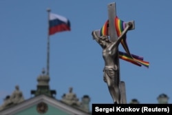 A rainbow-colored ribbon is tied to a crucifix next to a Russian flag fluttering atop the State Hermitage Museum in St. Petersburg last month.