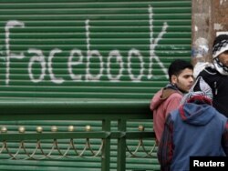 Opposition supporters talk near graffiti referring to the social networking site Facebook on Tahrir Square during the midst of the uprising in Cairo on February 5, 2011.