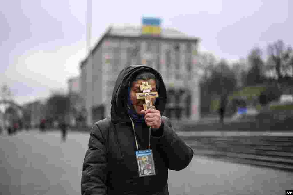 A woman holds a cross as she prays on Independence Square in Kyiv on the morning of February 24,