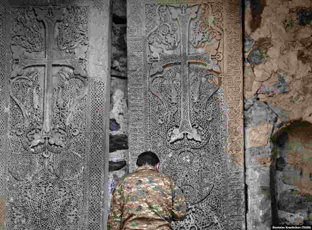 A man prays in front of Dadivank's large cross stones. 