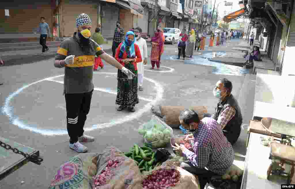 People in the Indian city of Jalandhar stand on designated areas to maintain social distancing as they wait to buy vegetables.
