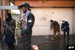 Taliban fighters stand guard as workers clean up following a deadly IS-K attack on a children's hospital in Kabul in November 2021.