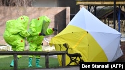 Members of the emergency services in green biohazard suits afix the tent over the bench on March 8 where a man and a woman were found on March 4 in critical condition in Salisbury.